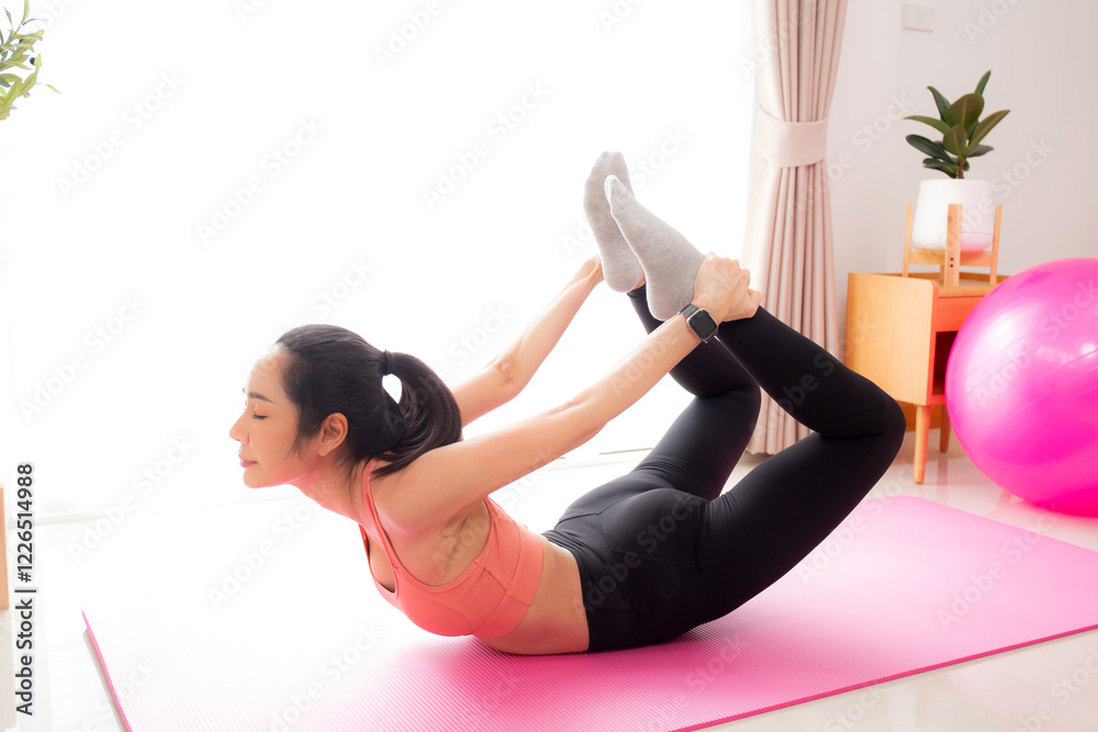 Fototapeta premium Young asian woman practicing Yoga with stretching muscle back on yoga mat in living room at home, woman exercise pilates with challenge and motivation, workout for wellness, sport and wellbeing.