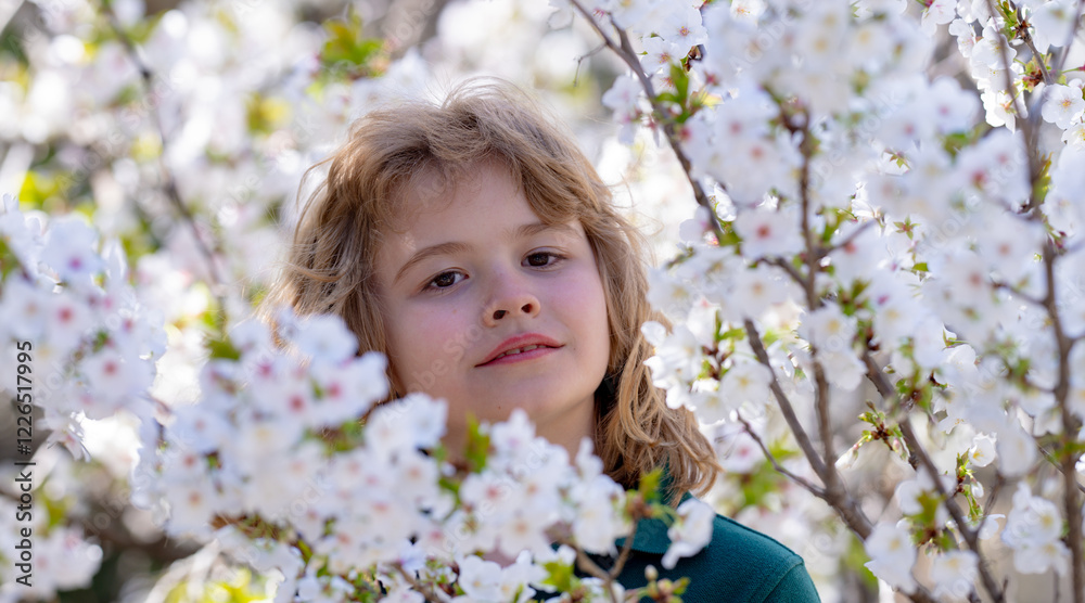 Little kid smelling spring flower outdoor. Portrait of smiling child face near blossom spring flowers. Kid among branches of spring tree in blossoms. Cute kids face surrounded by spring blossom Little kid smelling spring flower outdoor. Portrait of smiling child face near blossom spring flowers. Kid among branches of spring tree in blossoms. Cute kids face surrounded by spring blossom