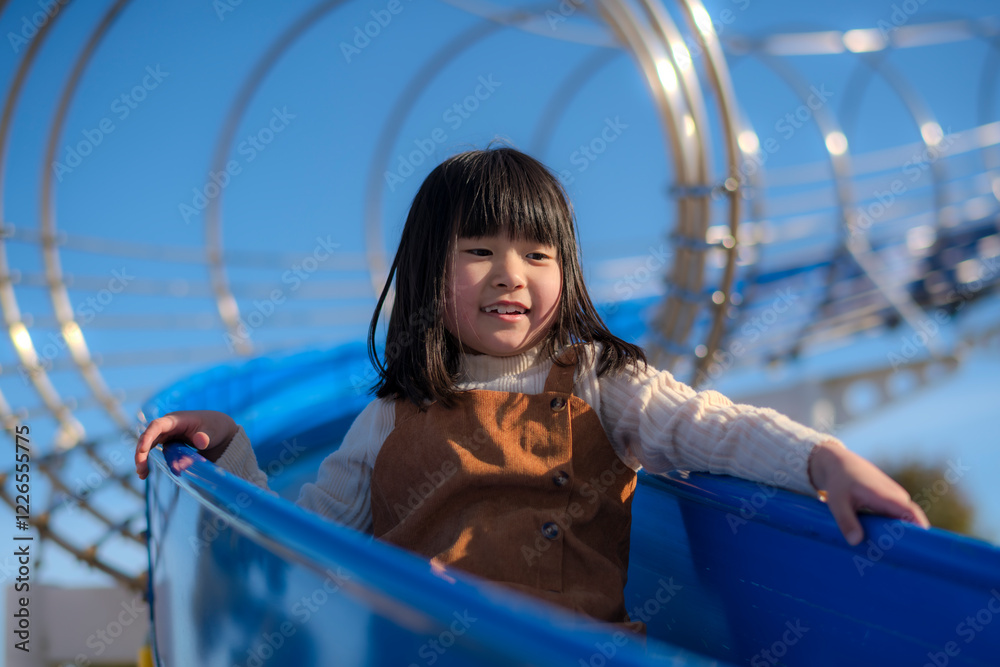 Obraz premium 公園の滑り台で遊ぶ元気な女の子