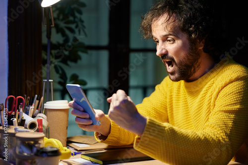 Man with a gesture of triumph while using the mobile in the office at night. photo