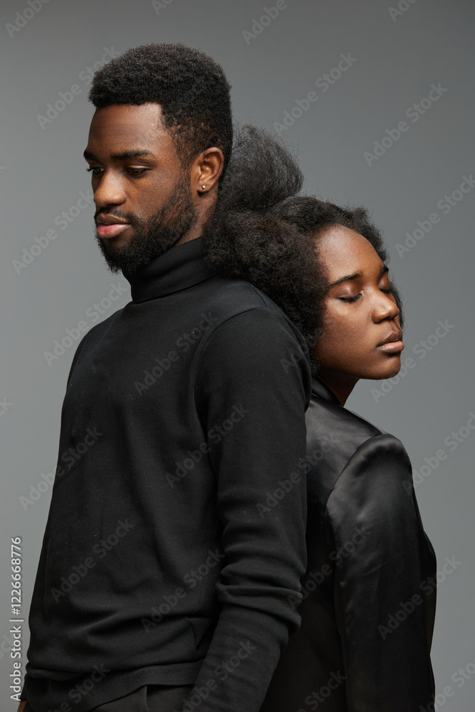 Obraz premium Portrait of a young Black couple dressed in stylish black attire, showcasing deep emotions against a neutral backdrop, perfect for conveying intimacy and connection