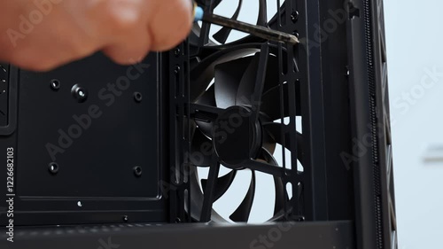 A computer technician unscrews a screw that secures a fan to a PC case. Assemble a computer system unit into a modern workstation. Upgrading rendering and gaming computer hardware components.