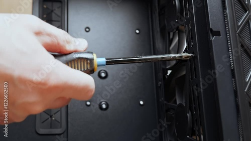 A computer technician unscrews a screw that secures a fan to a PC case. Assemble a computer system unit into a modern workstation. Upgrading rendering and gaming computer hardware components. 4k