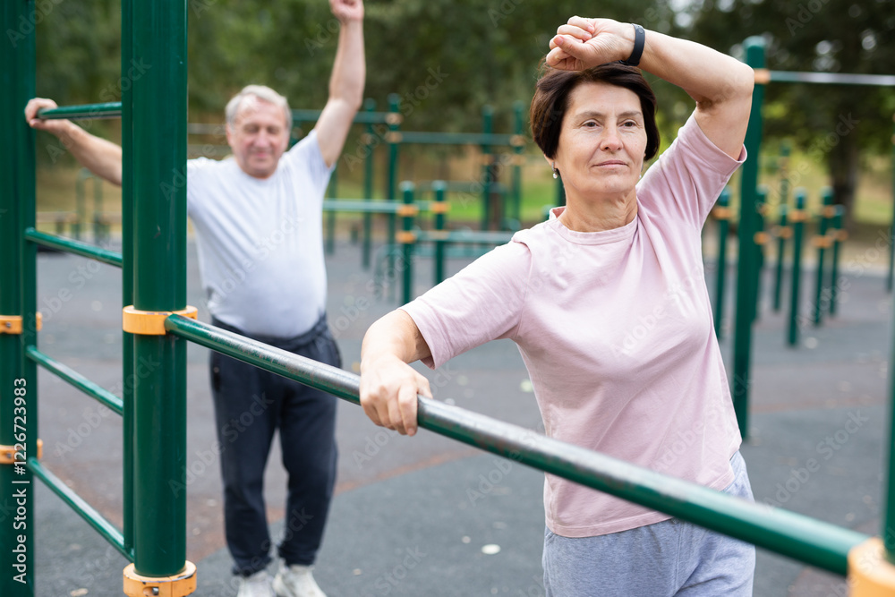 Obraz premium Healthy lifestyle in retirement - an elderly woman does a workout on the sports ground in park.