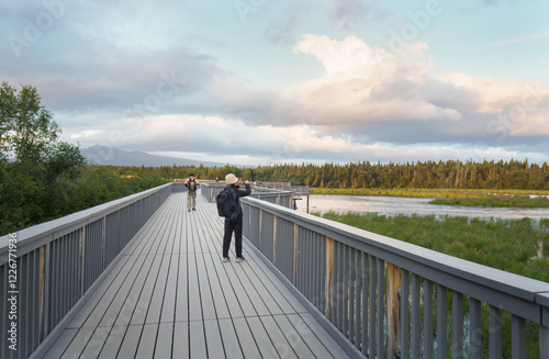 Obraz na płótnie Woman taking photos using a smartphone on the bear viewing platform. Brooks River. Katmai National Park. Alaska. w salonie