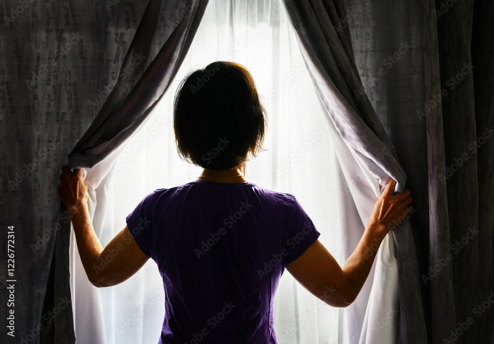 Woman opening the curtains and letting morning sunlight in. Bright sunny day outside.