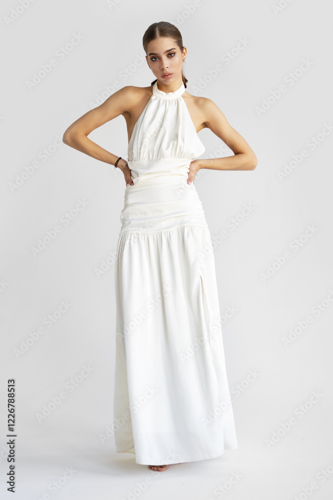 Young Beautiful Woman with dark hair stands and poses on isolated white background, wearing white maxi dress, looking in camera. Glamor fashion model. Beauty, skincare concept Young Beautiful Woman with dark hair stands and poses on isolated white background, wearing white maxi dress, looking in camera. Glamor fashion model. Beauty, skincare concept