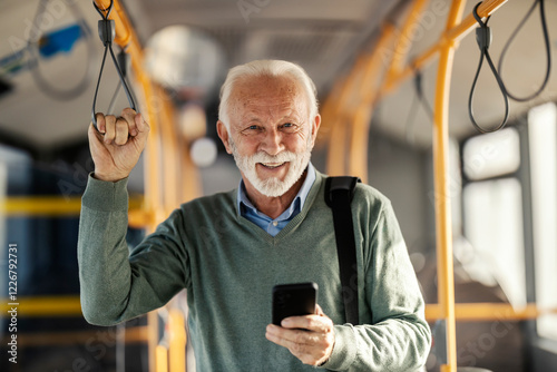 Portrait of an old commuter riding public bus and using his cellphone while smiling at camera. photo