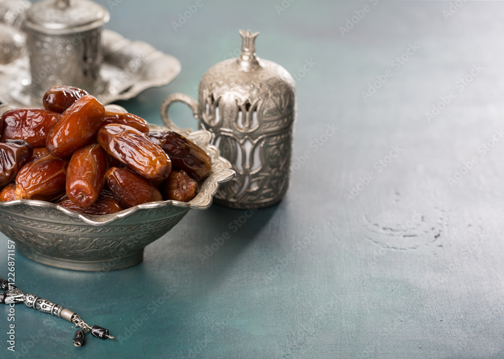 Bowl full of dates, cup of coffee and misbaha on blue-green wooden background