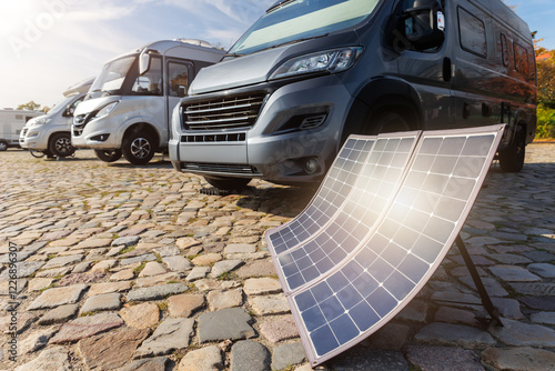 Many modern parked camper vans charge battery generator portable solar panels by clean eco energy, enabling off-grid travel freedom travel on sunny summer day. Innovative sustainability technology