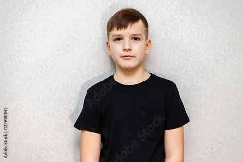 Portrait of a ten year old boy against a grey wall in a black T-shirt. photo