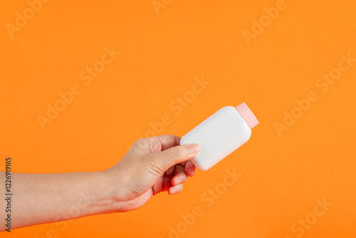 Baby talcum powder container in hand on orange background photo