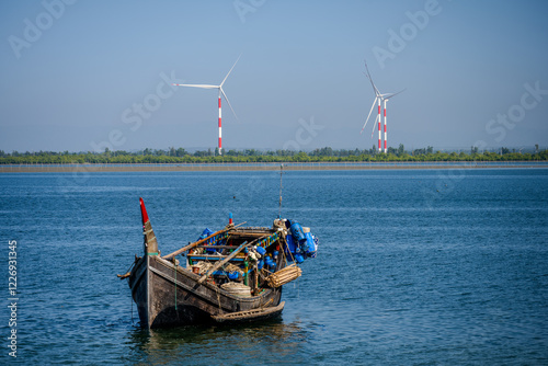 Fotografija Traditional Fishing Boat Floating on Calm Waters with Wind Turbines in the Backg