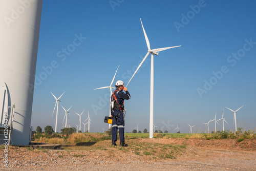 Engineer wearing uniform inspection and survey work in wind turbine farms rotation to generate electricity energy. Maintenance engineer working in wind turbine farm at sunset.