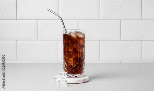 Cold brew coffee in a glass with ice and straw on a light table against a white brick background. photo