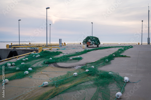 Heap of colourful trawling fishing nets and floats on the quay at harbour. Fishing nets on the harbor quay. Summer evening by the sea. photo