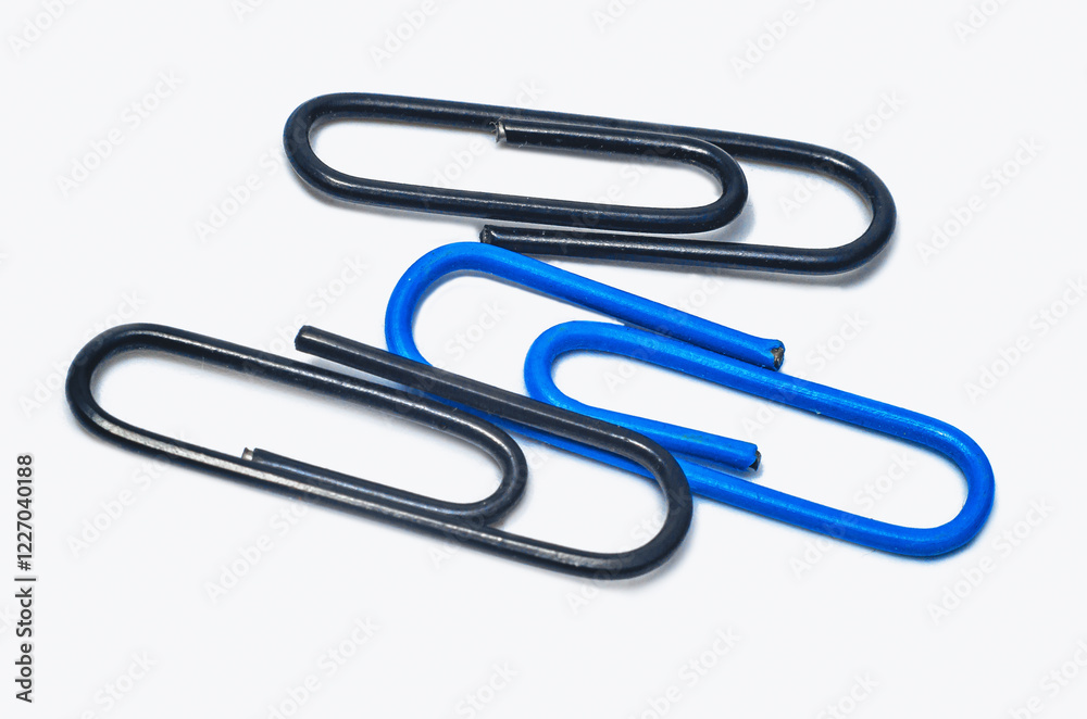 Two black and one blue paper clips lie on white background, isolated. Use of paper clips in stationery. Two black and one blue paper clips lie on white background, isolated. Use of paper clips in stationery.