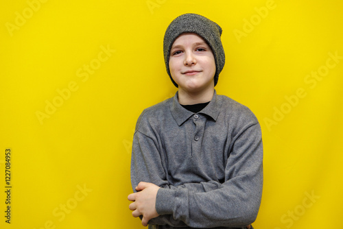 ten year old boy in grey knitted hat and sweater standing with arms folded on chest on yellow background photo