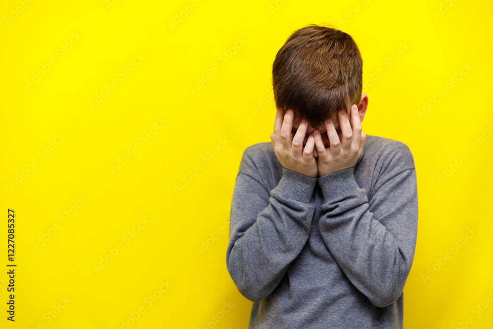 boy crying covering his face with both hands on yellow background