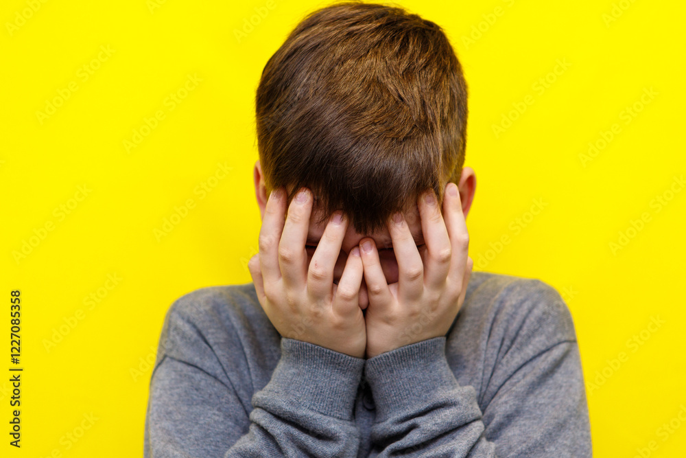 boy crying covering his face with both hands on yellow background boy crying covering his face with both hands on yellow background