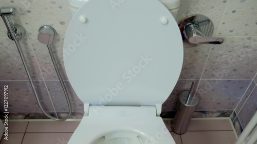 In the toilet, a man's hand presses the flush button on the toilet cistern, a strong stream of water flushes everything down the drain. Shot in motion