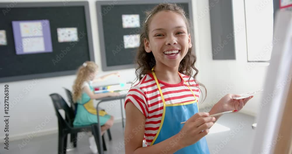 A biracial girl with beaming smile holds a paint palette in art class A biracial girl with beaming smile holds a paint palette in art class