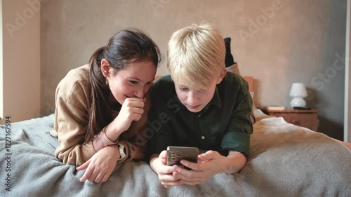 A brother and sister sit together, using their smartphones and laughing as they share funny videos or messages, enjoying their time together.