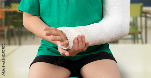 Close-up of a student boy suffering from a broken hand in a cast and sitting at the school desk