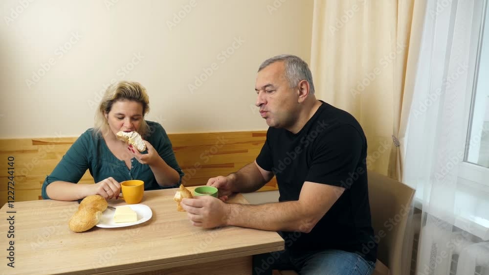 A man and a woman have breakfast at the kitchen table, drink coffee with rolls. A man and a woman have breakfast at the kitchen table, drink coffee with rolls.