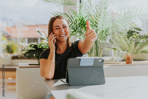 A woman is having a phone call and giving the thumbs up while working in the office, positive vibe
