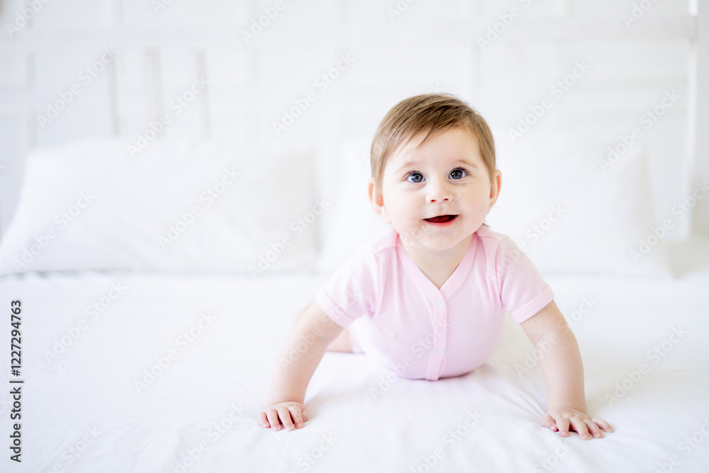 a six-month-old baby learns to crawl on a white cotton bed at home, a little baby girl in a pink bodysuit smiles, close-up a six-month-old baby learns to crawl on a white cotton bed at home, a little baby girl in a pink bodysuit smiles, close-up