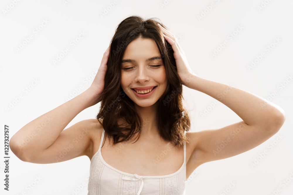 Young brunette woman in a white light top posing against a white background, expressing emotions and touching her face with her hands. Minimalistic and natural beauty concept Young brunette woman in a white light top posing against a white background, expressing emotions and touching her face with her hands. Minimalistic and natural beauty concept