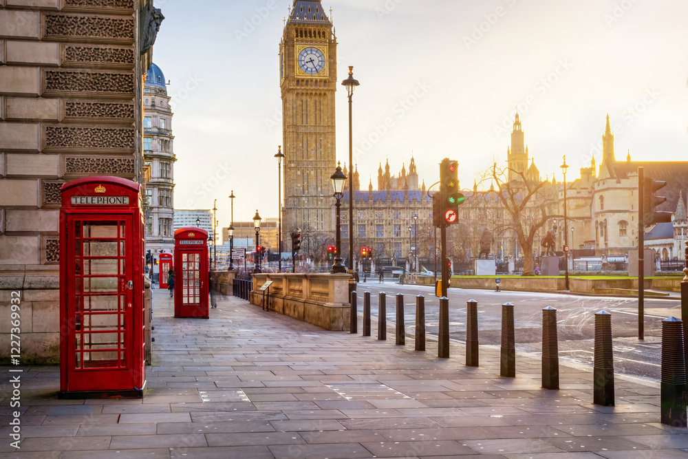 Beautiful sunrise view of the red telephone booths in front of the Big Ben clocktower in Westminster London, England, with blurred street traffic