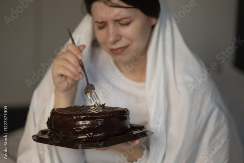 Sad single woman 25-30 years old struggling depression or stress wrapped in blanket eating sweets on sofa at home. Concept: stress psychological problems. Dismissal. Experiencing grief or bad news