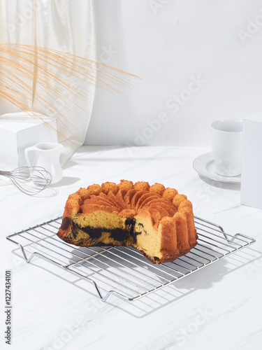 A striped bundt cake is cooling on a wire rack next to a cup and whisk, adding a delightful touch to a sunny kitchen setting