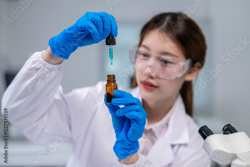 A woman in a lab coat is holding a bottle of blue liquid and a dropper