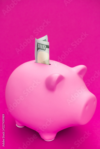 One hundred dollar bill in pink piggy bank with copy space. Close-up photo pink pig moneybox with dollars in it. Savings for retirement and personal finance concepts.