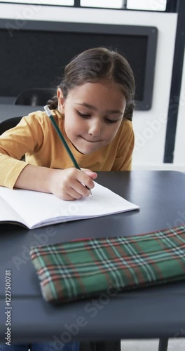 Vertical video: In a school setting, a young biracial student is focused on writing