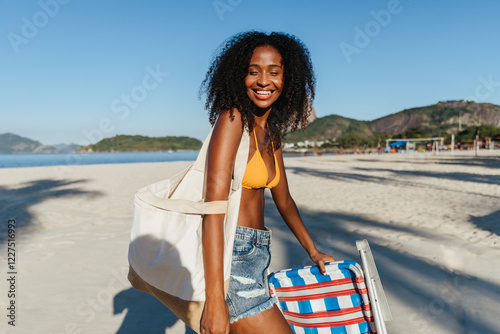 Smiling young woman in swimsuit with beach chair at sunny seaside