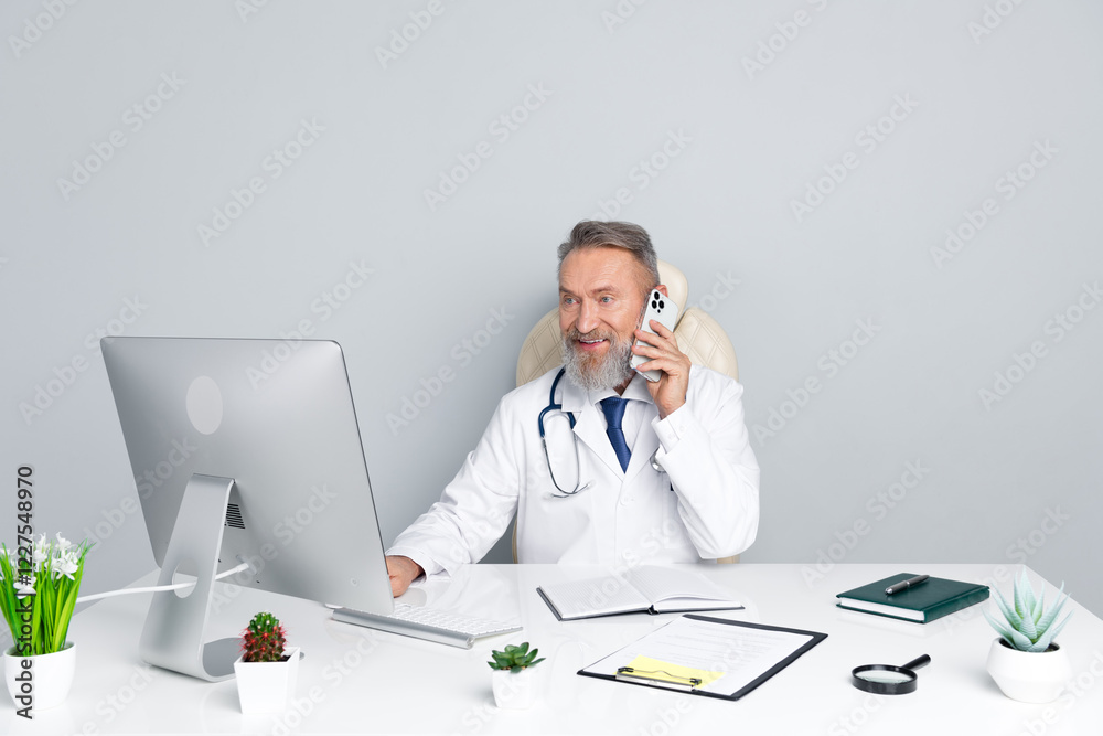 Elderly male doctor working at a desk in a modern medical office with a grey background Elderly male doctor working at a desk in a modern medical office with a grey background