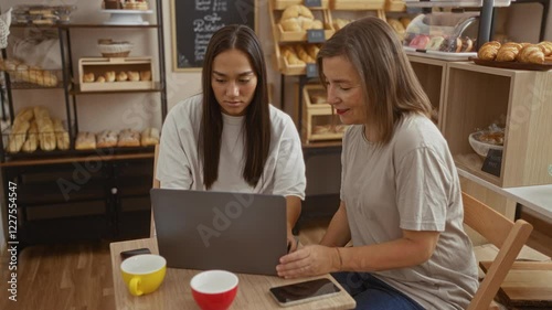 Wallpaper Mural Two women working on a laptop in a cozy bakery shop, surrounded by bread and pastries, enjoying coffee and casual conversation Torontodigital.ca