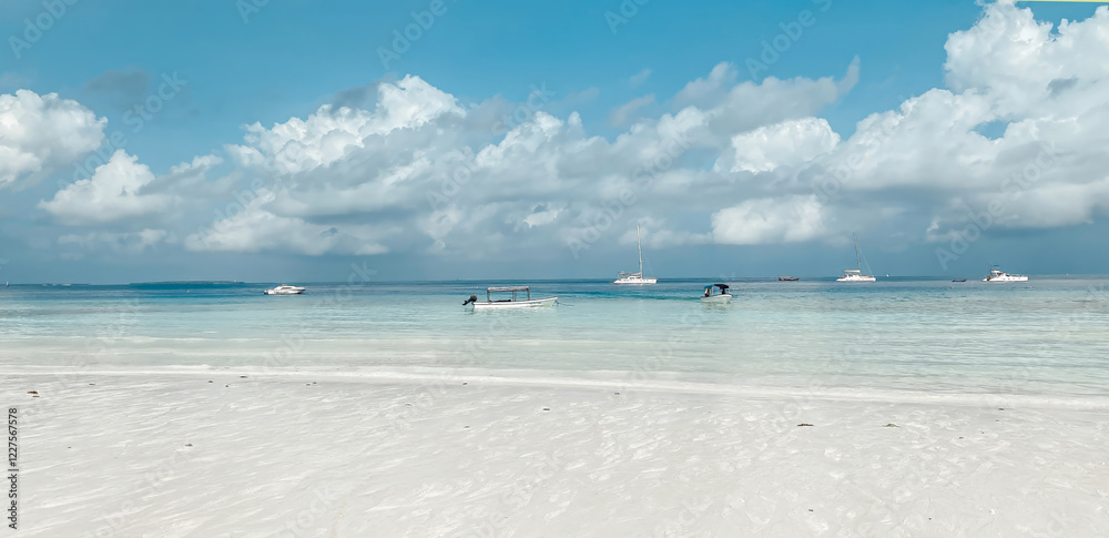 Fototapeta premium A beach with a few boats in the water. The sky is cloudy and the water is calm
