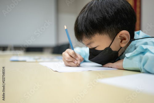 Asian boy wearing formal shirt and chemical face mask writing a test or exam for entering school. photo