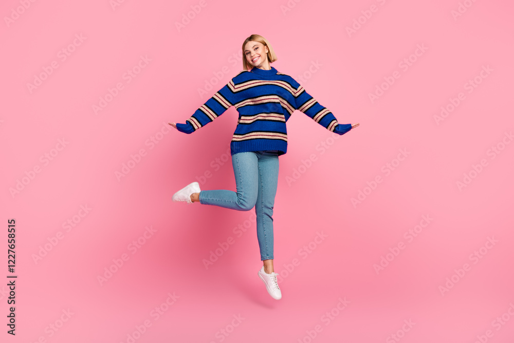Fototapeta premium Happy woman jumping cheerfully in casual attire against a vibrant pink background showcasing an enthusiastic gesture