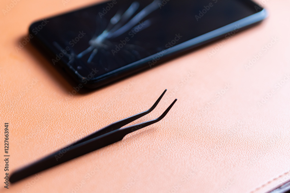 Broken Smart phone with Tweezers on Leather Surface