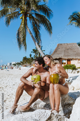 Hispanic young couple holding a coconut and having fun on caribbean beach in holidays or vacations in Mexico Latin America