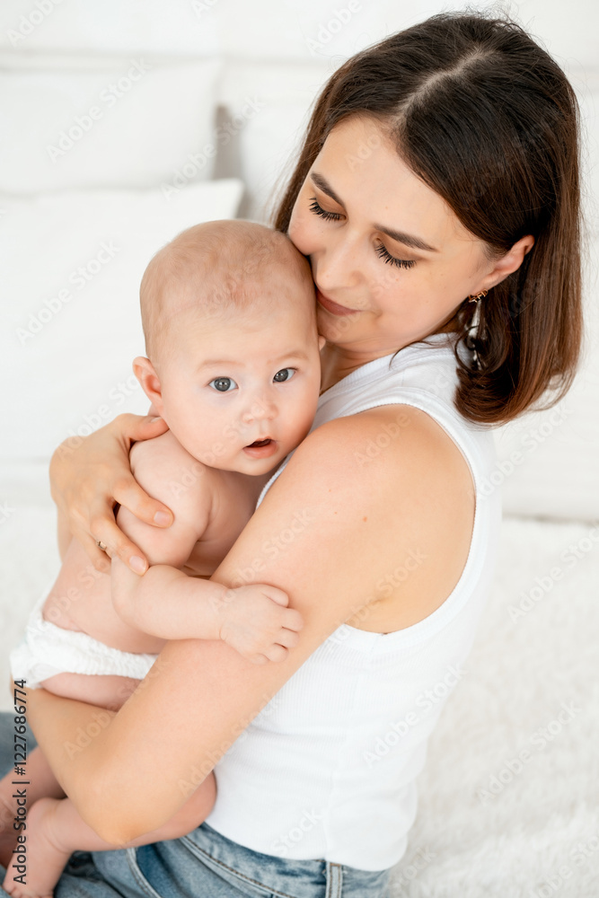 mom with a baby, an international family, a Caucasian mom with an Asian baby in her arms in the bedroom gently hugs him holding him in her arms, a place for text mom with a baby, an international family, a Caucasian mom with an Asian baby in her arms in the bedroom gently hugs him holding him in her arms, a place for text