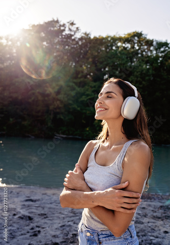 Young smiling woman with headphones enjoying healing music and sun embracing herself  photo