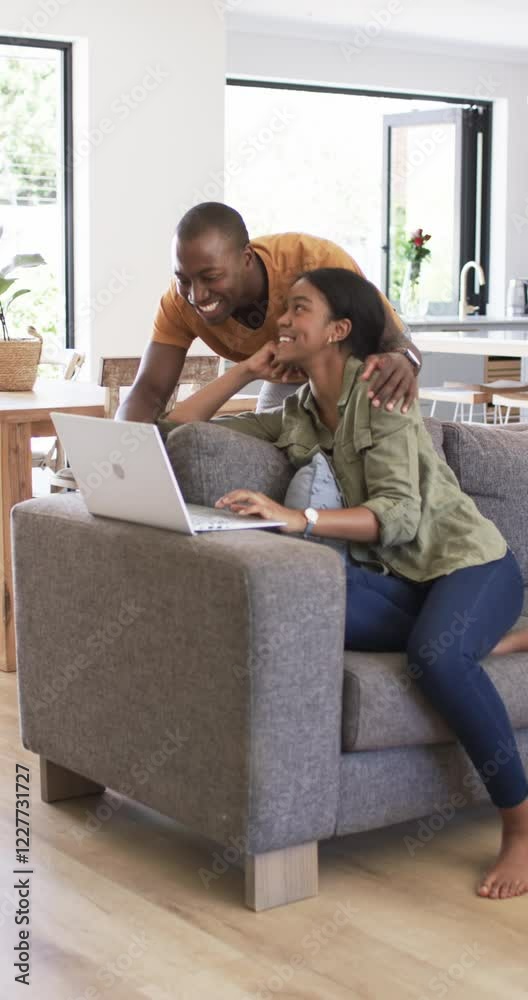 Vertical video: Couple relaxing at home, woman using laptop while man smiling and leaning on couch Vertical video: Couple relaxing at home, woman using laptop while man smiling and leaning on couch