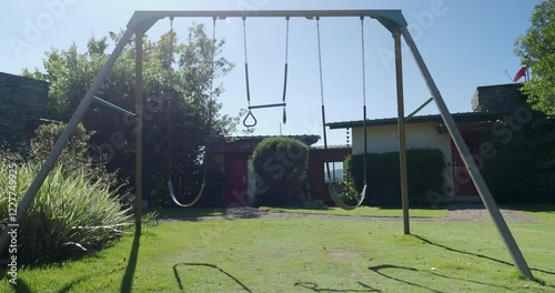 Empty children's playground at the backyard with swing swinging during sunny daytime. 